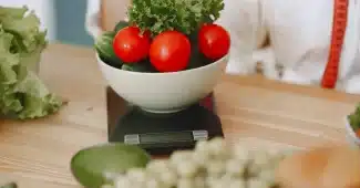 Fourchette et cuillère en équilibre sur une balance avec des légumes frais, symbolisant l'équilibre calorique quotidien.