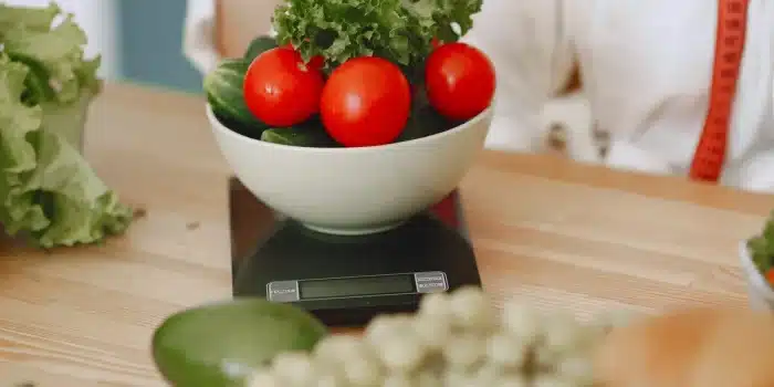 Fourchette et cuillère en équilibre sur une balance avec des légumes frais, symbolisant l'équilibre calorique quotidien.