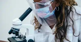 Mains gantées manipulant des échantillons en laboratoire devant un microscope et du matériel médical