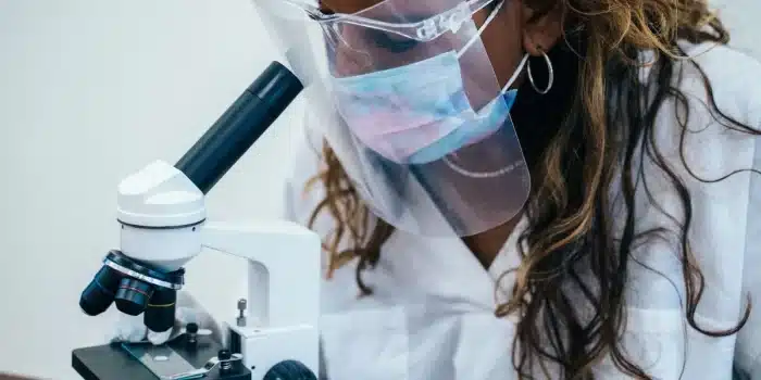 Mains gantées manipulant des échantillons en laboratoire devant un microscope et du matériel médical