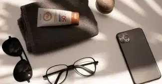 Accessoires de protection solaire à la plage : chapeau, lunettes de soleil, crème solaire et bouteille d'eau