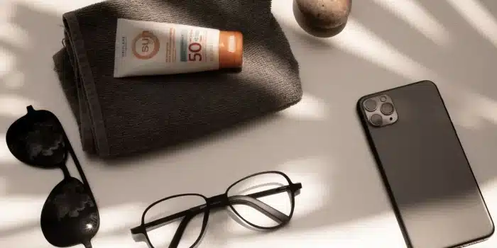 Accessoires de protection solaire à la plage : chapeau, lunettes de soleil, crème solaire et bouteille d'eau
