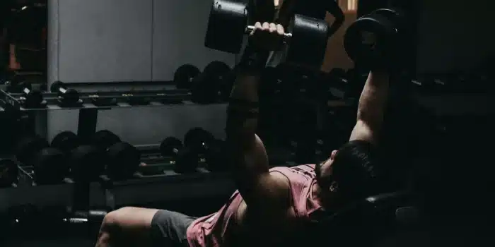 Personne effectuant un exercice de renforcement musculaire avec haltères en salle de sport