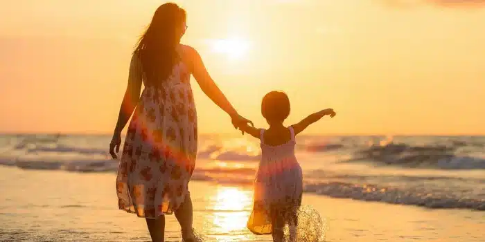 Parent guidant un jeune enfant avec des jouets et un livre près d'une tablette dans une pièce baignée de lumière