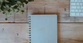Table de cuisine en journée avec carnet de suivi et tasse, mains anonymes