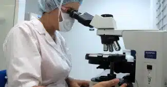 Mains gantées manipulant une pipette près de plaques cellulaires et d'un séquenceur en arrière-plan