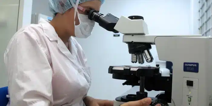 Mains gantées manipulant une pipette près de plaques cellulaires et d'un séquenceur en arrière-plan
