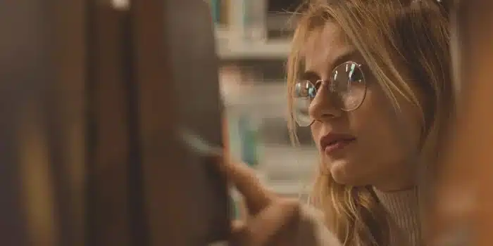 Élève peinant à lire et écrire, entouré de documents et de livres ouverts sur un bureau encombré.